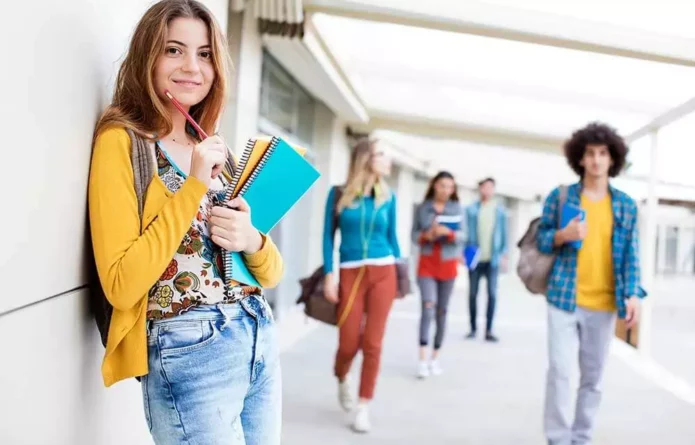Eine Gruppe jugendlicher Schüler mit Schulheften und Rucksäcken vor einem Schulgebäude, die von Kinesiologie profitieren durch mehr Motivation und weniger Prüfungsängsten.